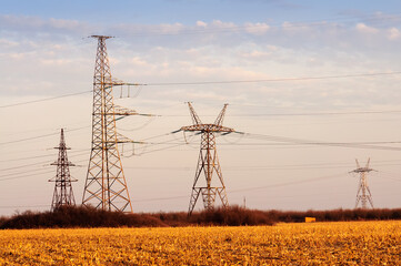 High-voltage pylons supplying electricity to the city, evening photo at sunset in an orange field