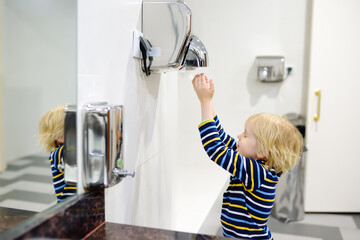 Child using restroom. Little boy dries his hands in the toilet with an automatic dryer. Taking care of the hygiene of children in public places. Healthy habits