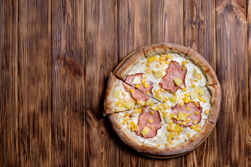 Delicious pizza with ham, pineapple, corn on a creamy base on woden background. Hawaiian pizza