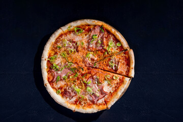 Delicious pizza with mozzarella cheese, ham, leeks on a tomato base on black background