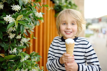 Happy little boy eating tasty ice cream cone outdoors during family stroll. Child have a snack on...