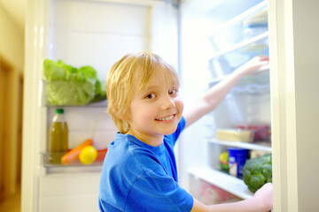 Cute preteen boy independently taking products from refrigerator at home. Child choosing between...