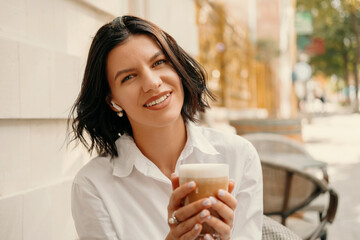 Close up portrait of a smiling woman holding a glass of late outdoors.
