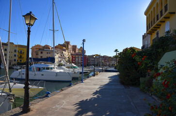 Yacht near Jetty. Yachts and motor boats in marina Port Saplaya, Valencia. Yacht and fishing motorboat in yacht club. Colourful houses with apartments at coast Mediterranean Sea. Sailboat near pier.