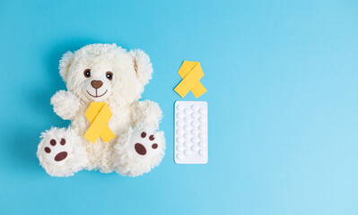 Toy bear with a yellow ribbon and pills on a blue background.