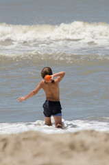 boy playing with a ball on the beach, in the sea waiting for the waves on vacation