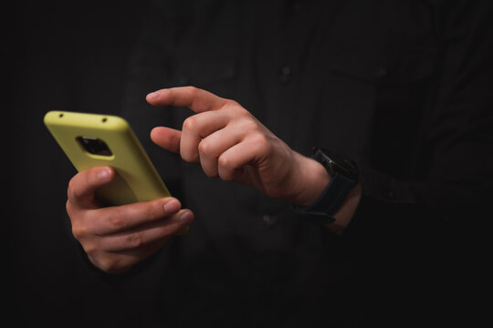man dressed in black, checks his smart phone with a gesture in his hand to perform an action, black background