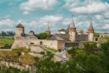Fototapeta na wymiar Famous historical fortified old medieval castle of Kamianets-Podilskyi in Ukraine, ancient fortress and tourist attraction with towers, thick walls, bridge in summer day, blue sky with textured clouds