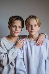 Two happy boys, happy brothers who are smail together. Brothers sit on grey background. modern tenagers. book cover. hug each other