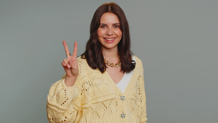 Hipster pretty woman in cardigan showing victory v sign, hoping for success and win, doing peace...