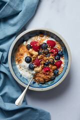Breakfast of Greek yogurt with cashews, blueberries and raspberries, sprinkled with apple crumble on a blue tablecloth