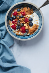Breakfast of Greek yogurt with cashews, blueberries and raspberries, sprinkled with apple crumble on a blue tablecloth
