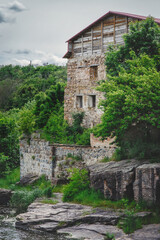 Scenic view: ruins of abandoned water mill in ancient granite canyon Buky in Ukraine in summer, lots of plants, rocks, stones, trees, moss, river around; mysterious scenery on overcast day, vertical 