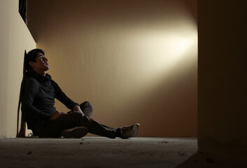Hombre joven triste, sentado en el suelo mirando arriban y pensando con iluminación puntual hacia...