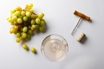 Glass of white wine, green grapes and corkscrew on white background, with copy space