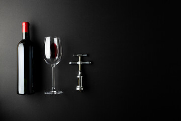 Bottle of red wine, glass and corkscrew on black background, with copy space