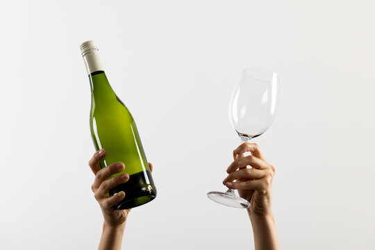 Hands holding bottle of red wine and glass on white background, with copy space