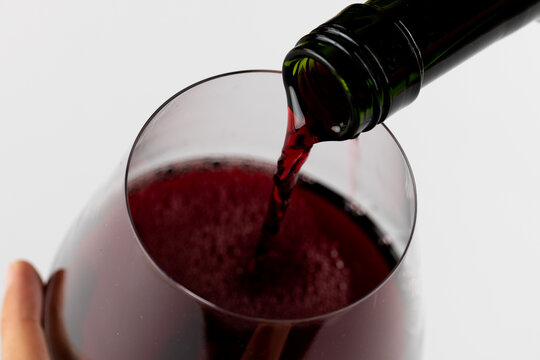 Hands holding bottle of red wine and glass on white background, with copy space