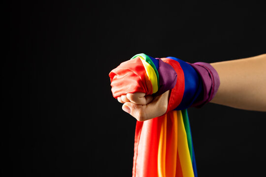 Hand holding rainbow coloured flag with copy space on black background