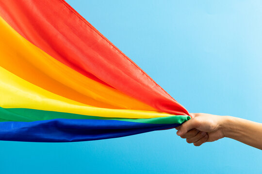 Hand holding rainbow coloured flag with copy space on blue background