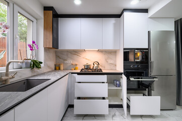 A spacious and updated kitchen with a white color scheme, a marble floor, an open ovens door, and...
