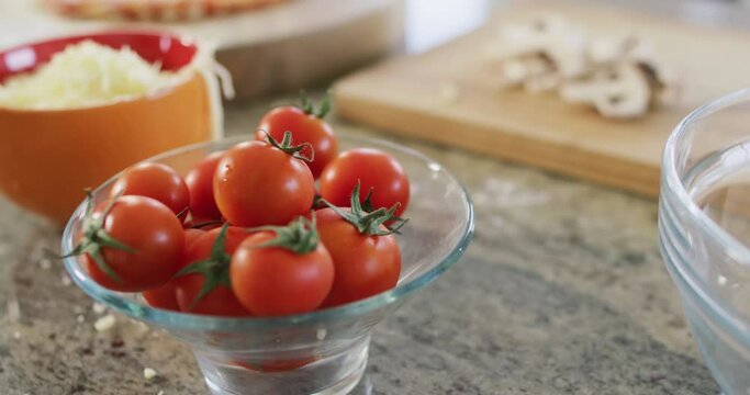 Bowls of tomatoes, grated cheese with sliced mushrooms, pizza ingredients in kitchen, in slow motion