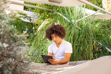 A young ethnic man digital tablet outdoors in a green area in nature. Free green open space place to work, business, study, freelancer coworking, in nature. Environmentally friendly working 