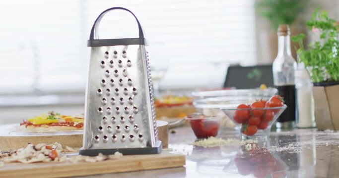 Cheese grater, tomatoes and sliced mushrooms, pizza ingredients on kitchen counter