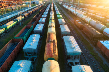 Drone view of freight trains at sunset. Colorful railway cargo wagons with goods on railroad....