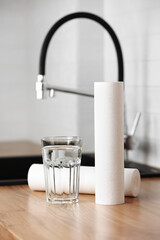 A glass of clean water and foamed polypropylene filter cartridges on wooden table in a kitchen...