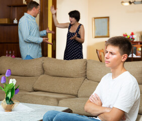 Obraz premium Adult spouses quarrelling while their teenage son sitting offended on sofa