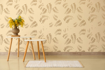 Vase with mimosa flowers on table near beige wall in room
