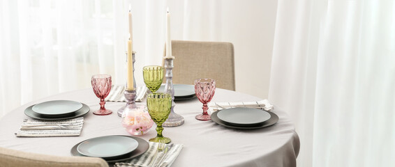 Burning candles with dinnerware and cutlery on table in room