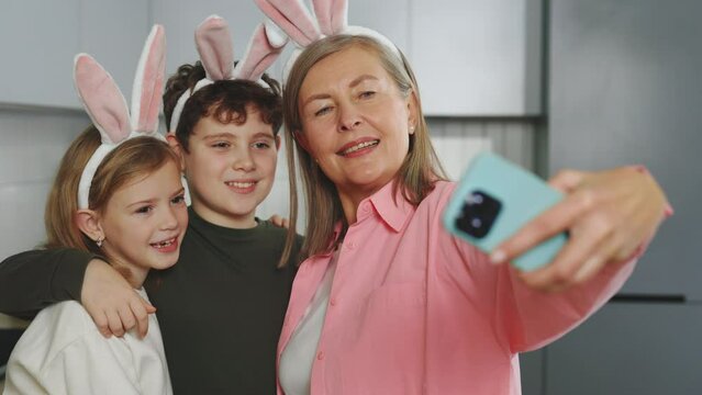 Happy grandmother with grandchildren doing selfie with easter eggs, wearing bunny ears, have beauty and fun day together at home. Happy easter. Concept of childhood, tradition, family weekend