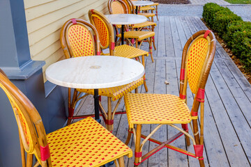 Bright orange and red plastic wicker bistro chairs surround white table outside a coffee shop.