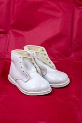 A old pair of white leather baby boots on a red background.