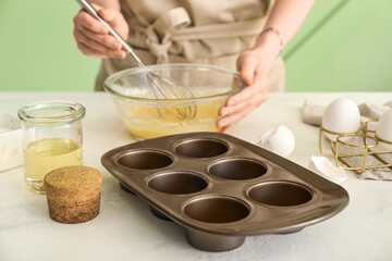 Woman preparing delicious muffins at table in kitchen