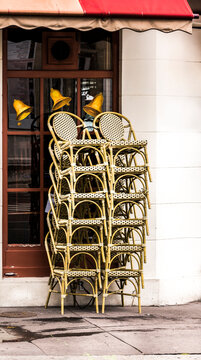 A stack of wicker chairs sit on a sidewalk outside a cafe in Paris France.