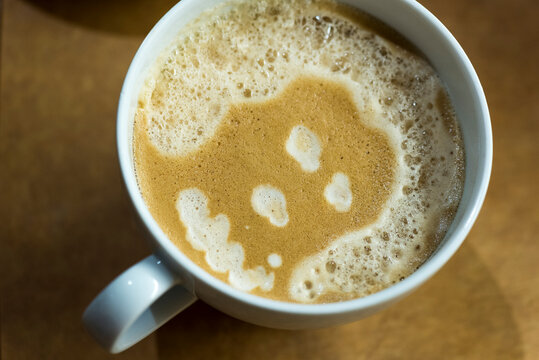 A face with curly hair is formed by the bubbles in the foam of a latte.