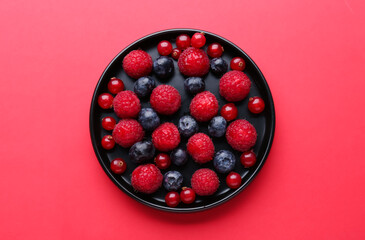 Plate of fresh berries on red background