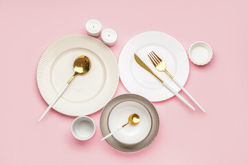 Different clean dishware with golden cutlery on pink background
