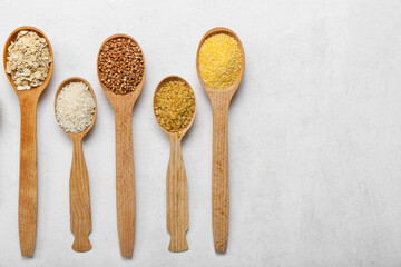 Wooden spoons of different cereals on light background