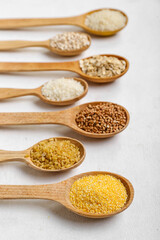 Wooden spoons of different cereals on light background, closeup