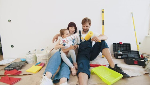 Repair in the apartment. Family smiling and posing. Happy family renovating their home. Close up of happy young family spending time together resting after painting and renovating room