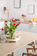 Vase with tulips, Easter eggs and jug of water on dining table in kitchen