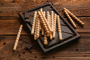Cutting board with tasty wafer rolls, coffee beans and chocolate on wooden background