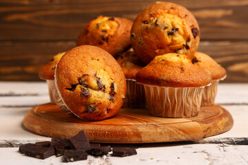 Board with delicious muffins and chocolate on white wooden table