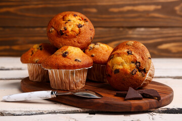 Board with delicious muffins and chocolate on white wooden table