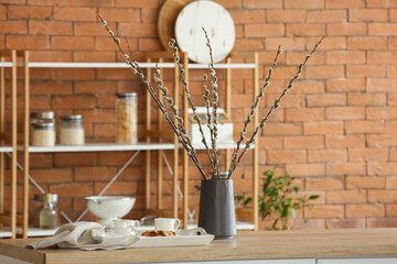 Vase with willow branches and breakfast on counter in kitchen