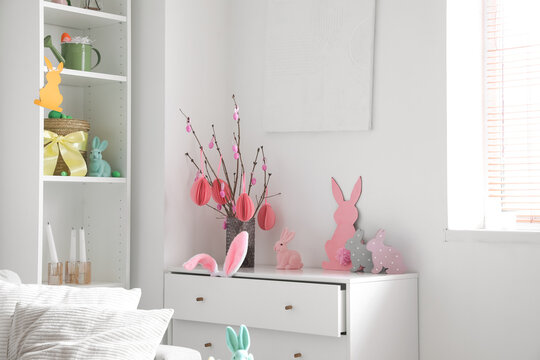 Vase with tree branches, Easter eggs and rabbits on chest of drawers in living room